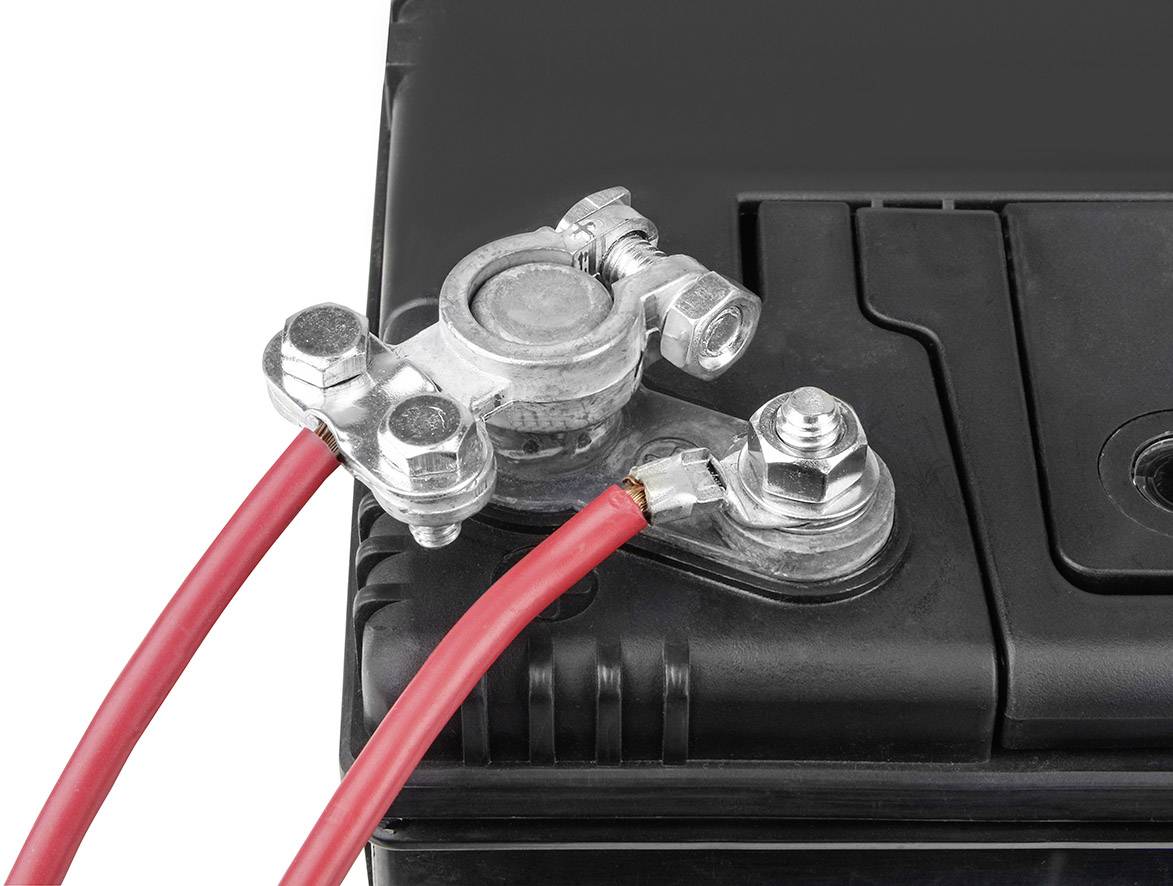 Schwarze Autobatterie mit roten Kabeln, die an den Klemmen befestigt sind.