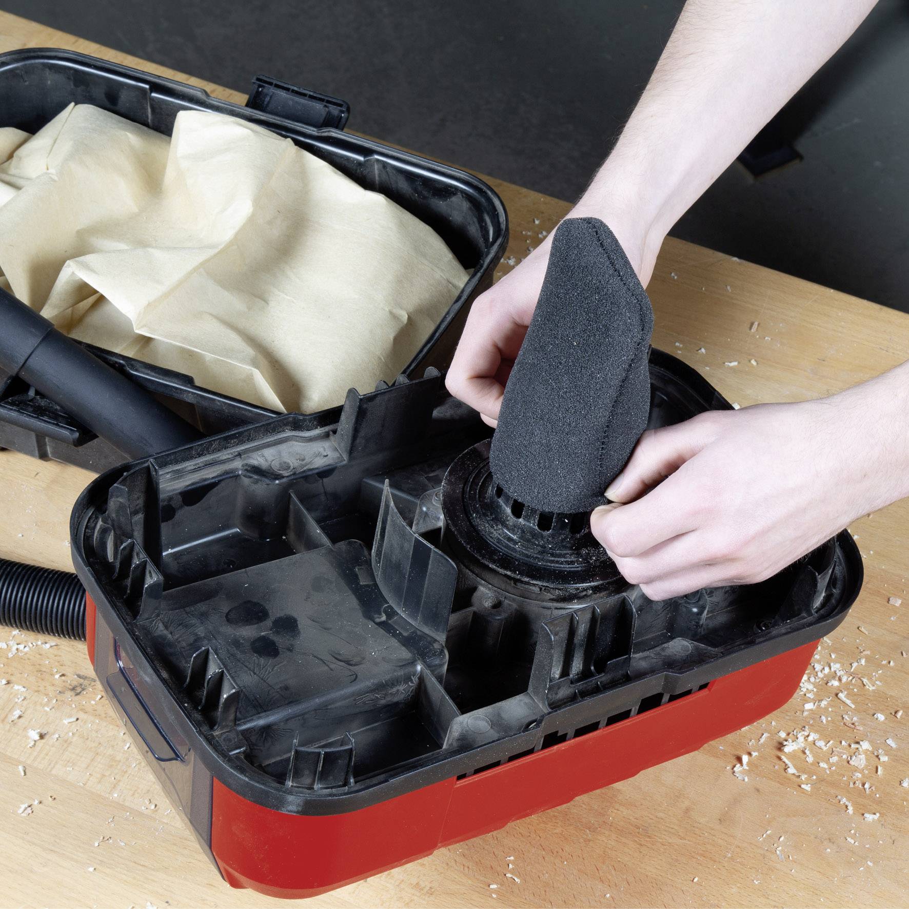 Eine Person wechselt den Filter eines Staubsaugers. Der Staubsauger ist offen, und der alte Filter ist sichtbar auf einem Holztisch.