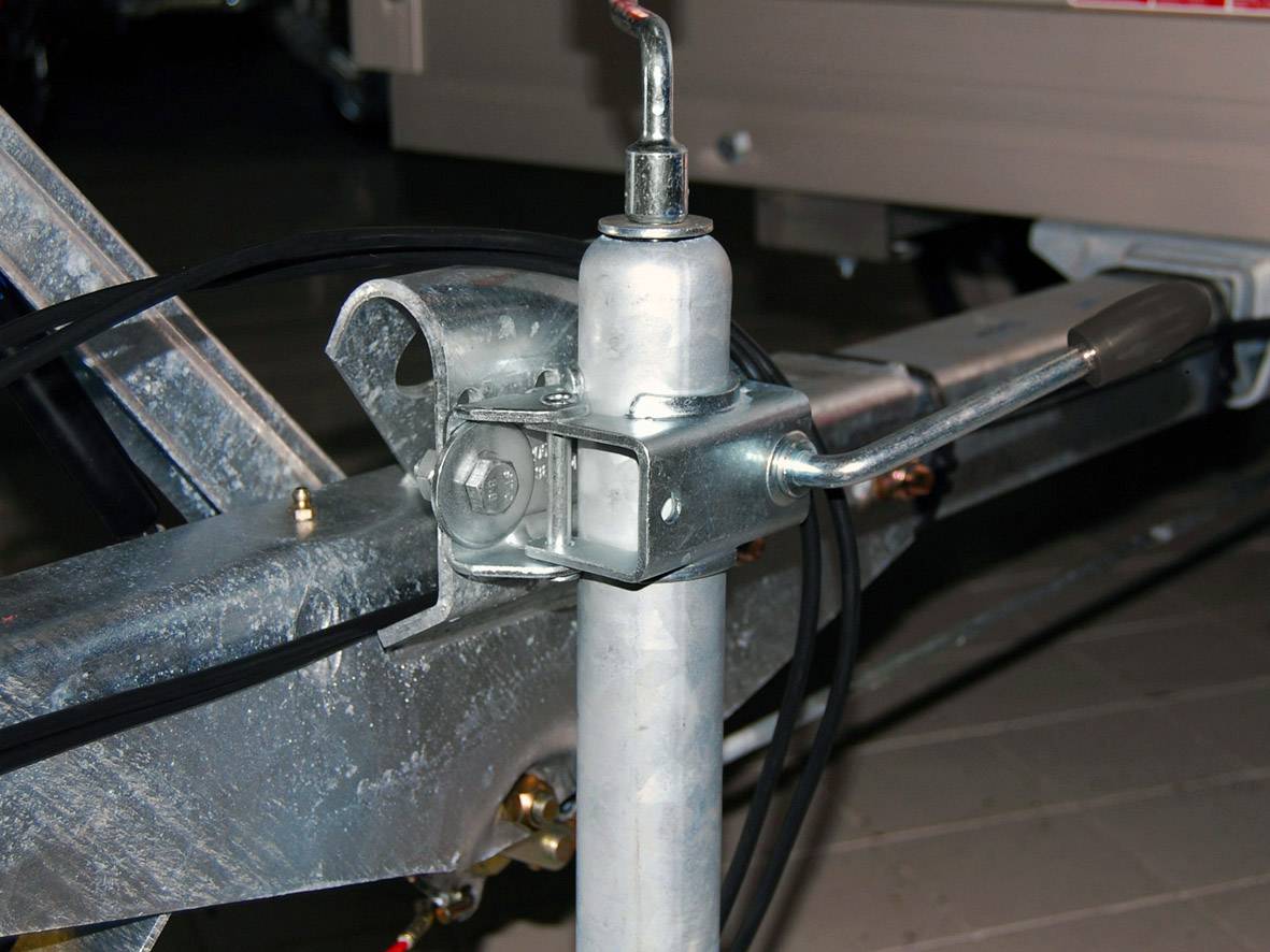 'Nahaufnahme einer Metallkurbel am Anhänger. Die Kurbel ist mit einem Stahlrahmen verbunden und dient zur Stabilisierung oder Anpassung der Stützlast.'