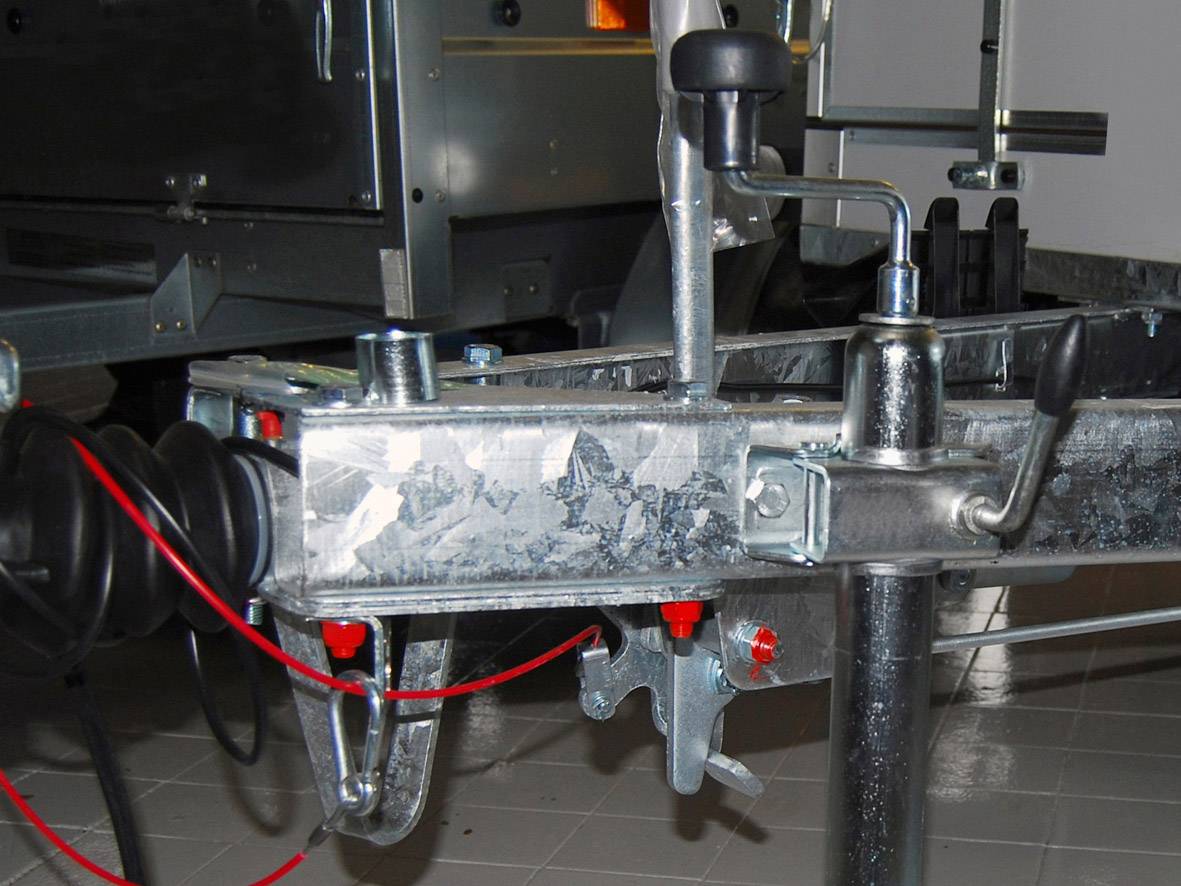 Ein Metallanhänger-Kupplungsmechanismus mit Hebel und Kabeln, abgestellt auf einem gefliesten Boden.