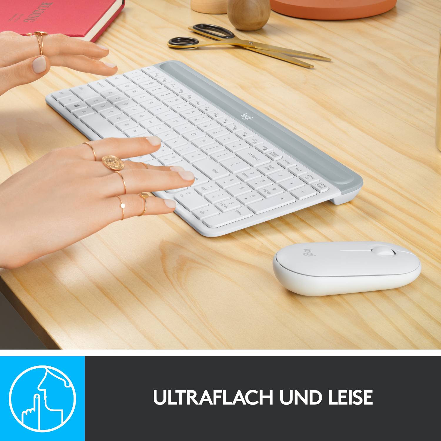 Auf einem Schreibtisch liegt eine flache, weiße Tastatur. Daneben eine Hand, eine Maus, eine Kaffeetasse und ein rotes Notizbuch.