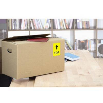 Ein brauner Karton mit einem gelben 'TOP'-Aufkleber steht auf einem Holztisch. Im Hintergrund sind Bücherregale zu sehen.