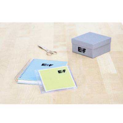 Notizbuch, CD-Hülle und Schachtel mit 'E1F'-Logo auf einem Tisch. Eine Schere liegt daneben.