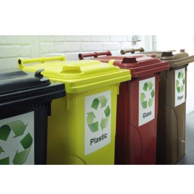 Mehrere farbige Mülltonnen mit Recycling-Symbolen und Beschriftungen: 'Plastic', 'Glass', 'Paper', aufgereiht vor einer Wand.