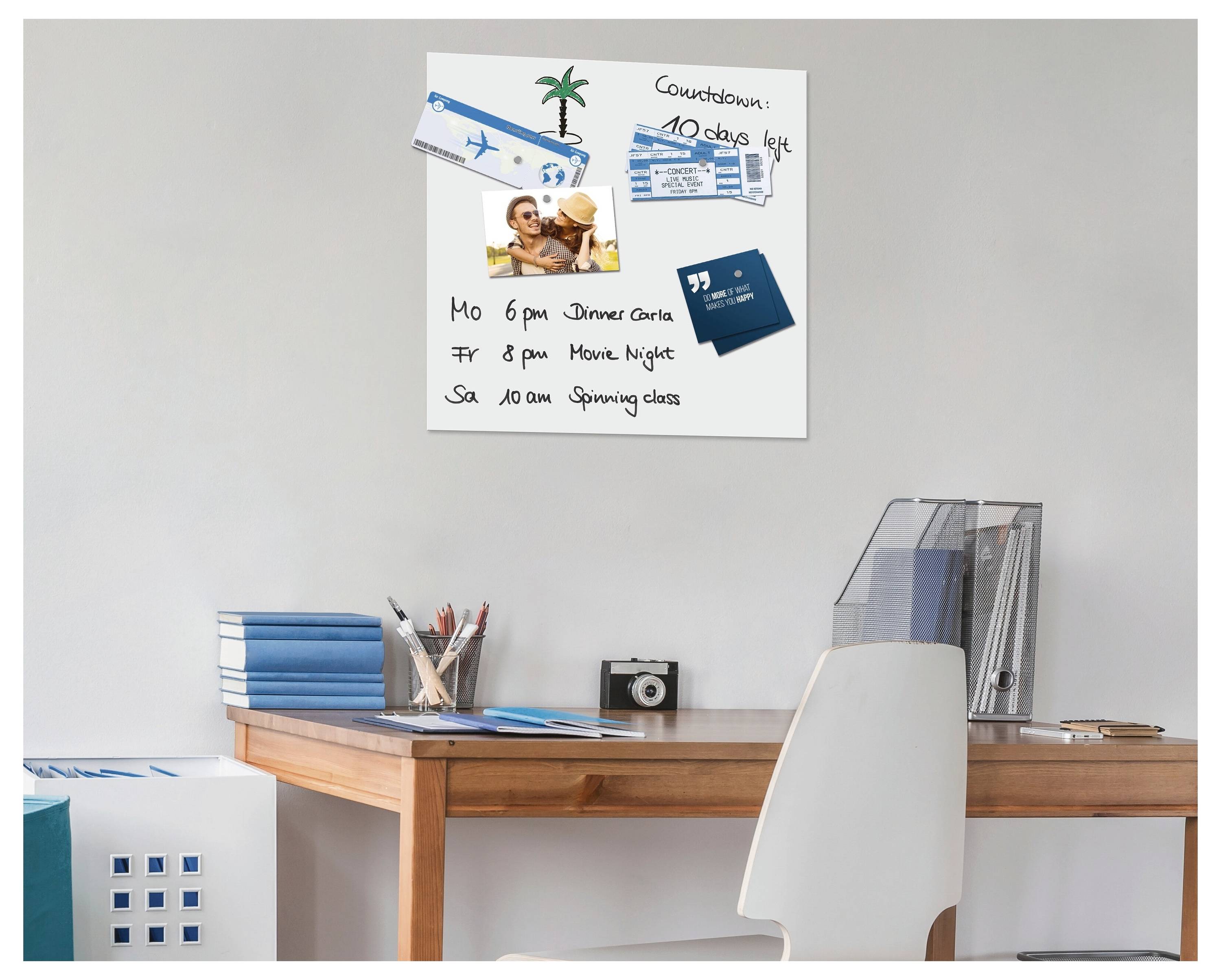 Ein Home-Office-Schreibtisch mit einem weißen Stuhl, Büchern, Zeitschriften, einer Kamera und einer Pinnwand an der Wand, auf der ein Countdown, Fahrkarten, Fotos und ein Wochenplan zu sehen sind.