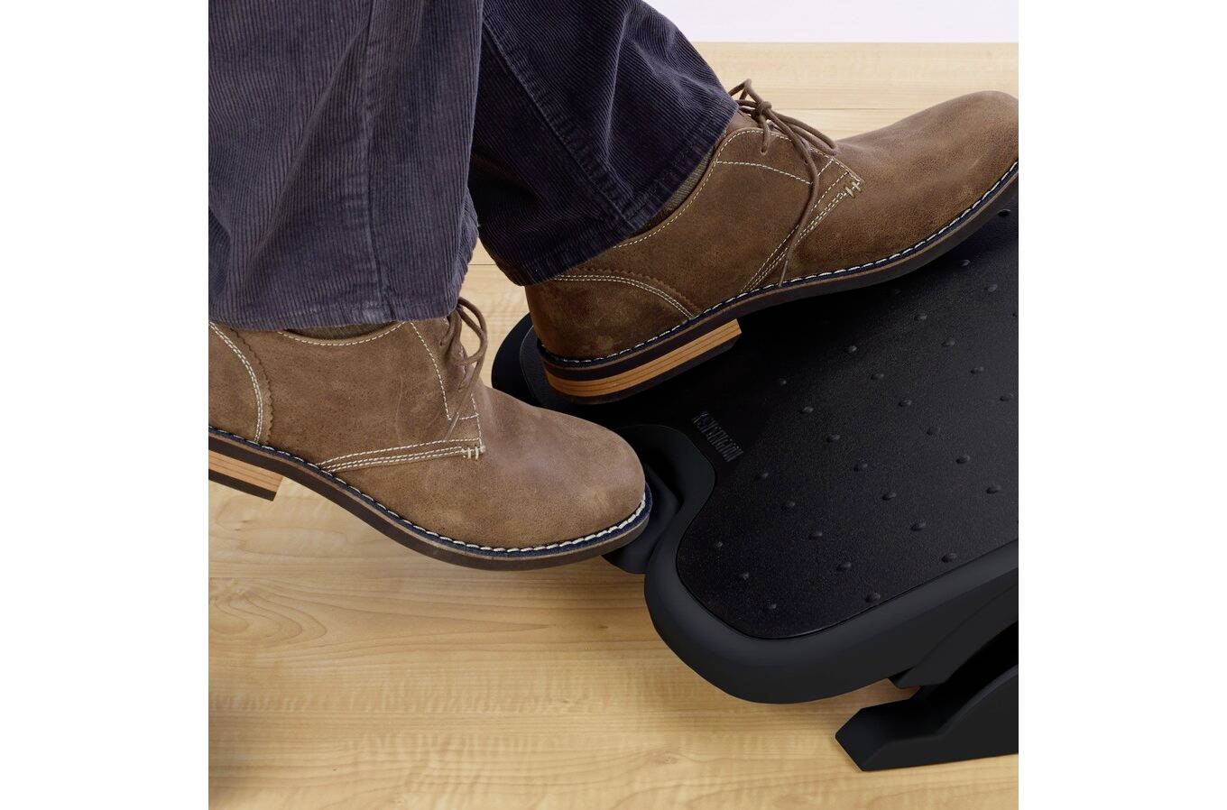 Eine Person mit braunen Schuhen betätigt einen Fußstützenpedalauf einem Holzboden und demonstriert dessen Verwendung zur Höhenverstellung der Fußstütze.