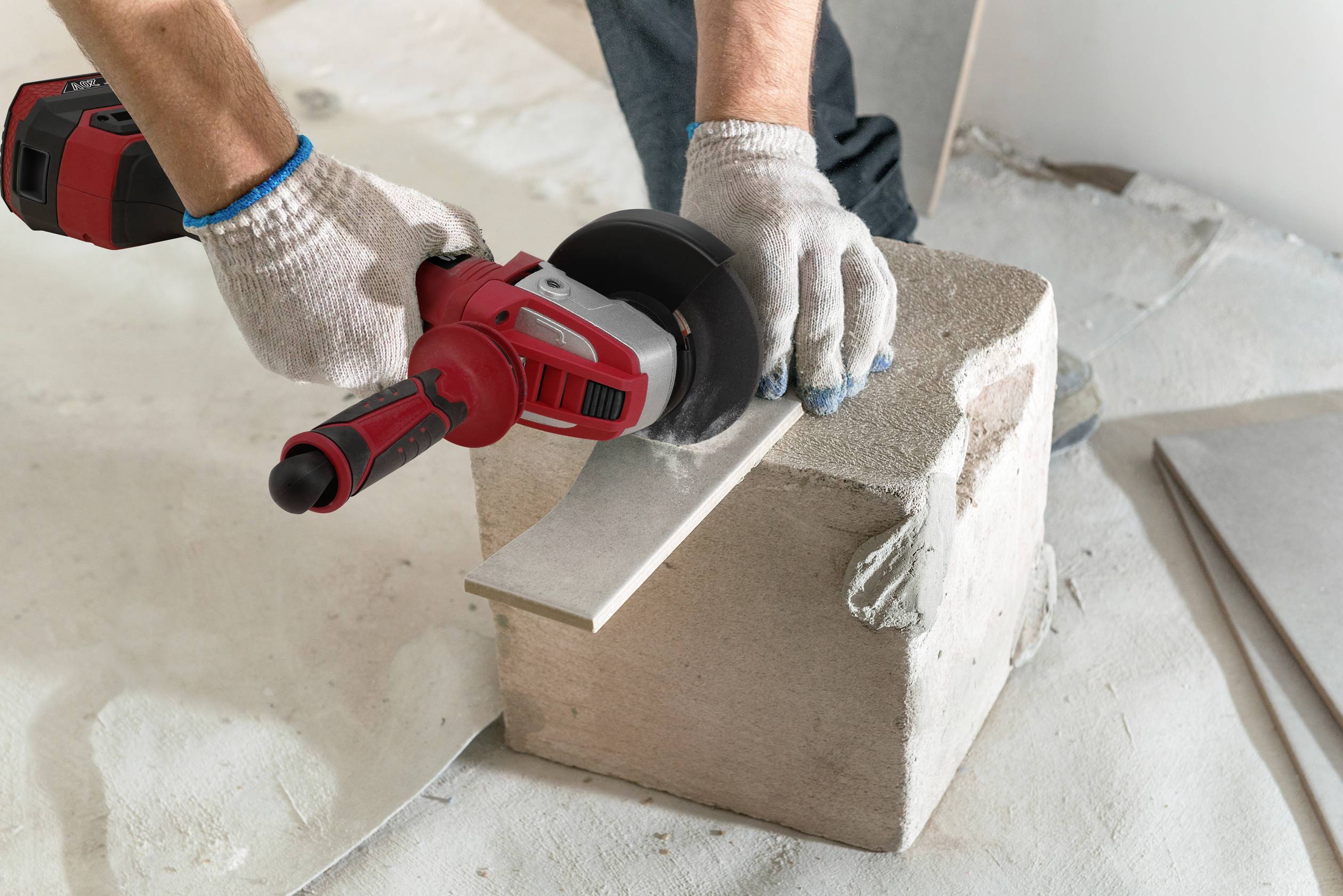 Ein Arbeiter in Handschuhen schleift mit einer elektrischen Schleifmaschine ein Metallstück auf einem Betonblock.
