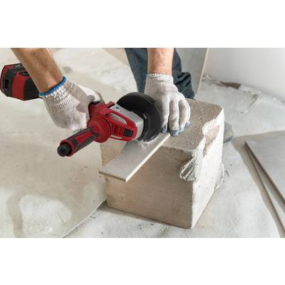 Ein Arbeiter in Handschuhen schleift mit einer elektrischen Schleifmaschine ein Metallstück auf einem Betonblock.