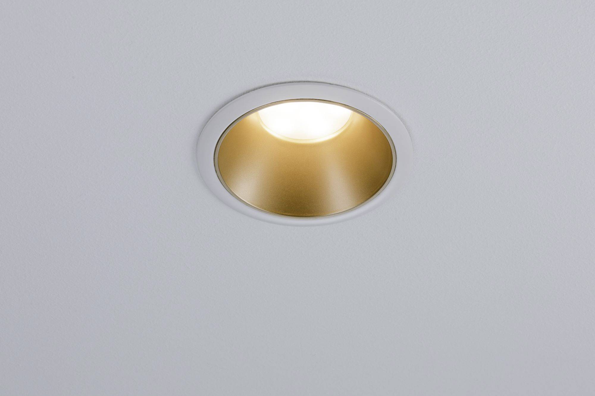 Eine einzelne goldene Deckenlampe leuchtet in einem schlichten, weißen Hintergrund.