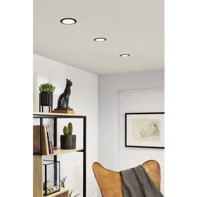 Moderner Wohnraum mit Lederstuhl, offenen Regalen, Zimmerpflanzen und Kunst an der Wand. Drei Deckenleuchten strahlen sanftes Licht.