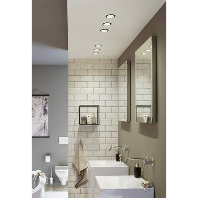 Badezimmer mit weißen Fliesen, zwei Waschbecken, Spiegeln und dunklen Wänden. Deckenstrahler beleuchten den Raum. Im Hintergrund eine Toilette.