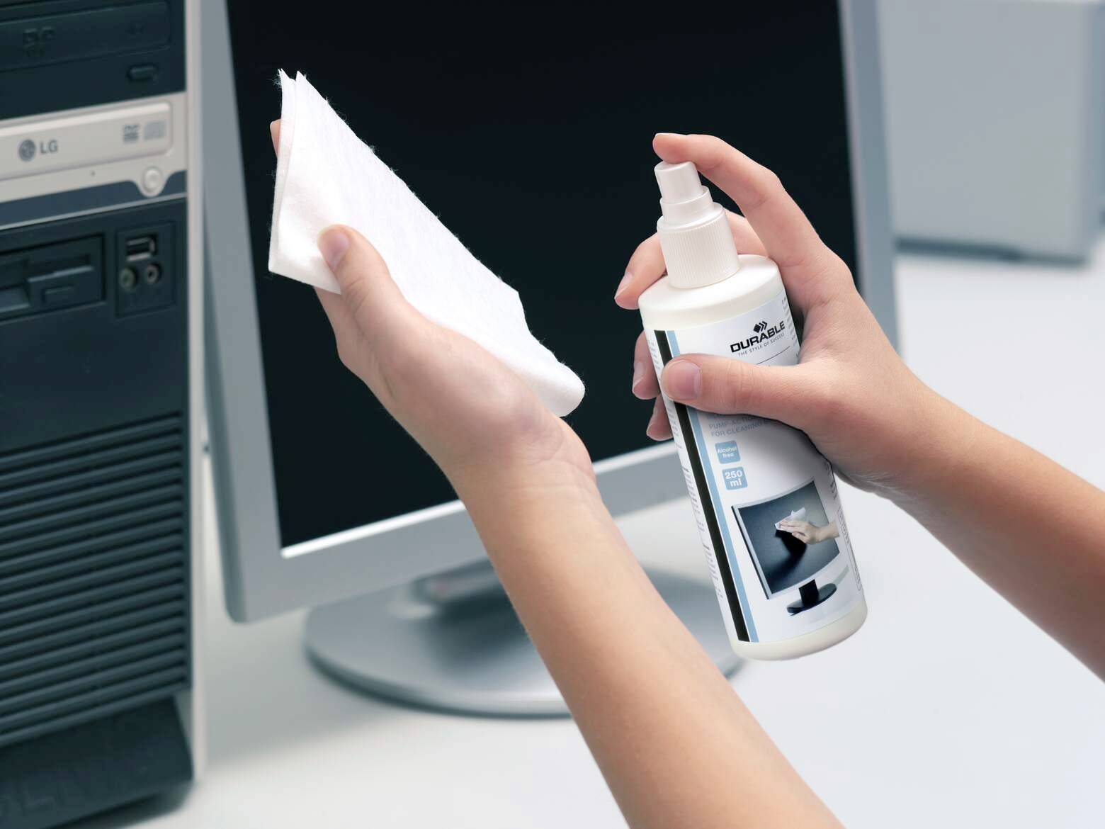Eine Person reinigt einen Computermonitor mit einer Reinigungslösung und einem Tuch. Der Computer ist ausgeschaltet und die Umgebung ist ein Bürosetting.