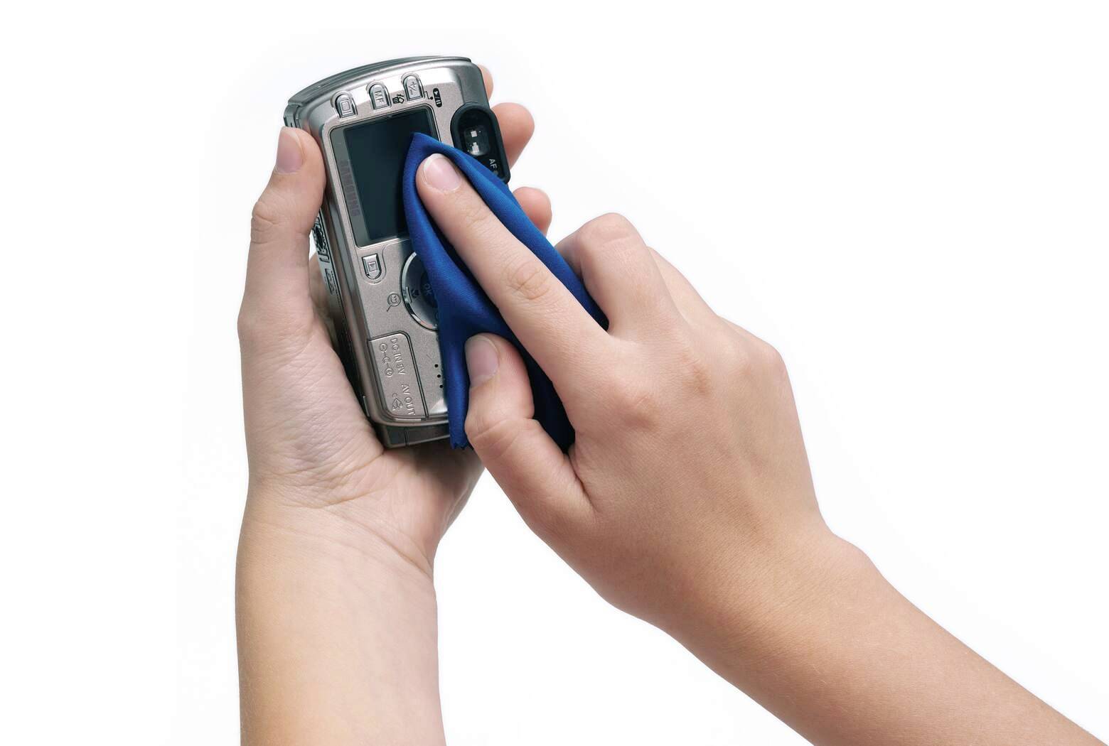 Zwei Hände halten eine Digitalkamera; eine Hand reinigt die Linse mit einem blauen Tuch.