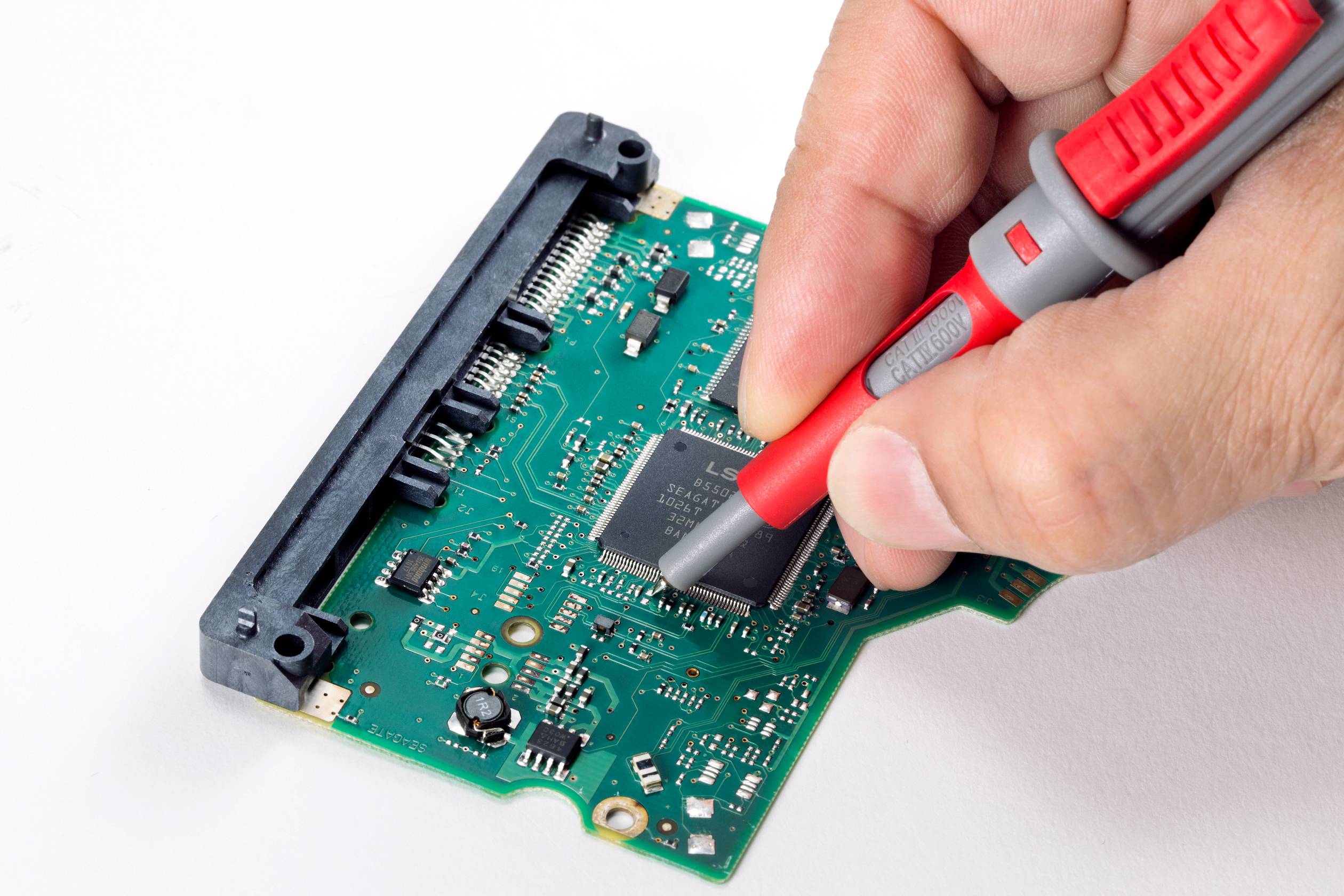 Eine Hand hält eine Prüfspitze und berührt die Schaltungen auf einer grünen Leiterplatte, die in einen Computer eingebaut wird.