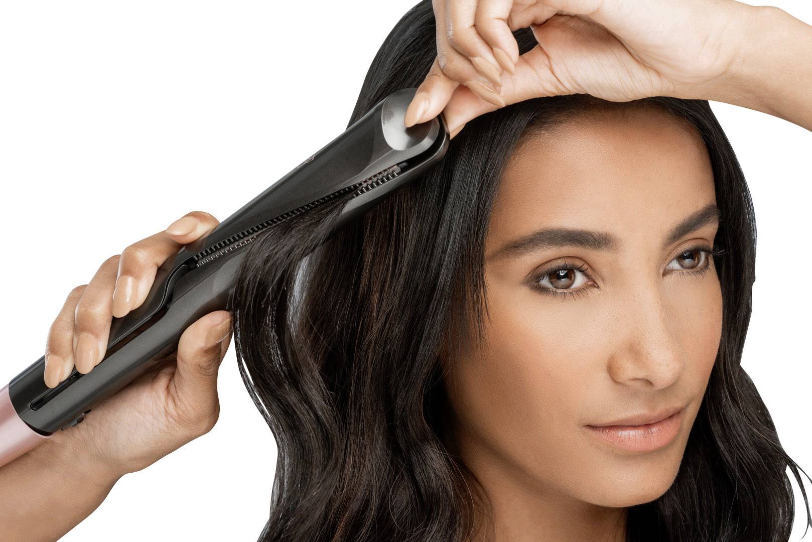 Eine Person glättet ihr schwarzes Haar mit einem Glätteisen. Die Szene zeigt den Prozess des Haarstylings aus nächster Nähe.