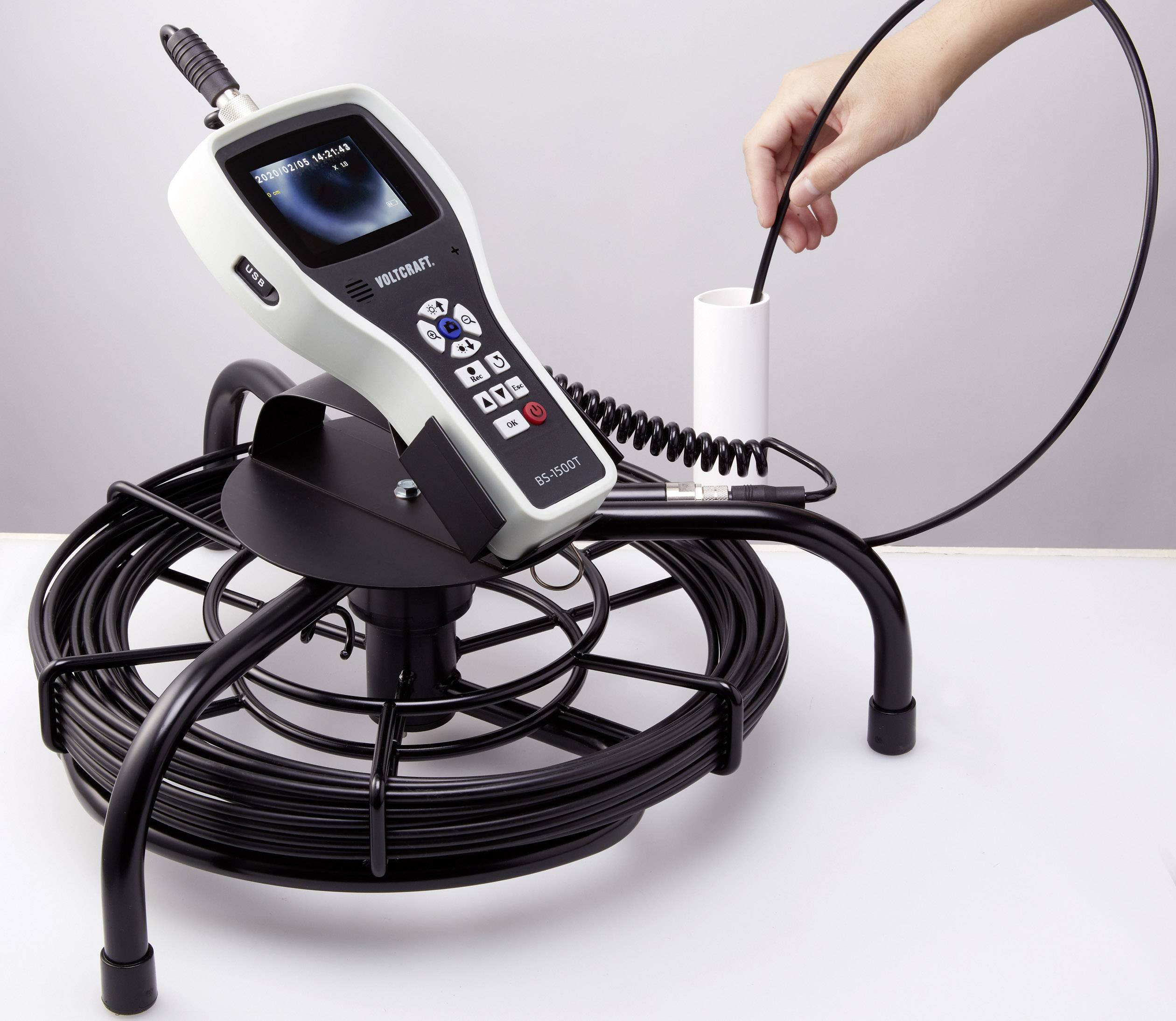 Ein tragbares Inspektionsgerät mit Bildschirm, spiralförmigem Kabel und Sonde, wird von einer Person zur Überprüfung eines Rohrs genutzt.