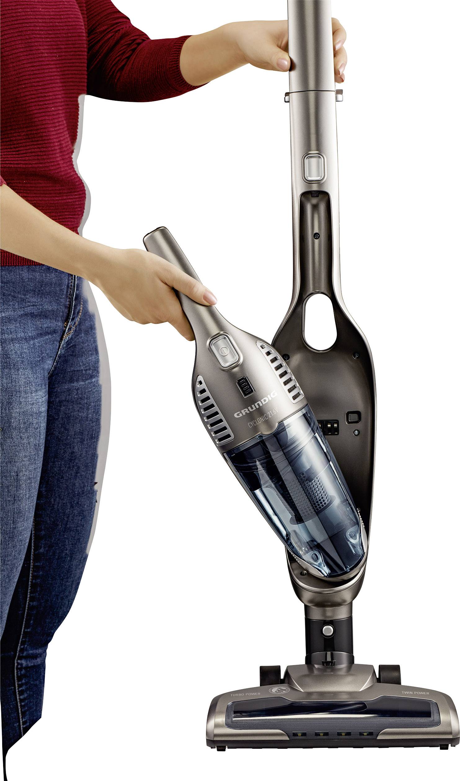 Eine Person entfernt einen Handstaubsauger von einem Staubsaugerständer. Der Staubsauger ist grau und wird mit einer Hand gehalten.