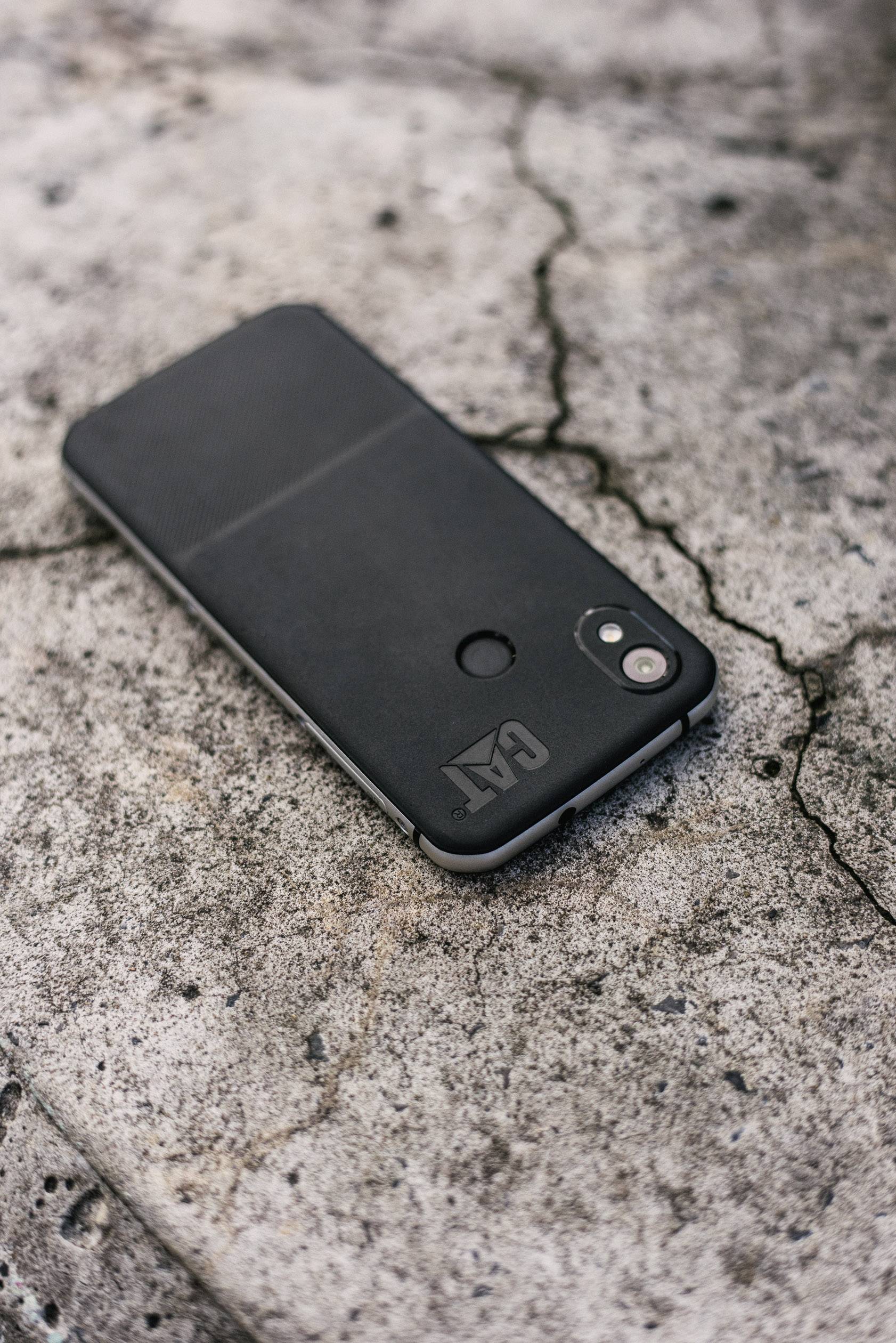 Ein schwarzes Smartphone mit einem schlichten Case liegt auf einem grob strukturierten, rissigen Betonboden.