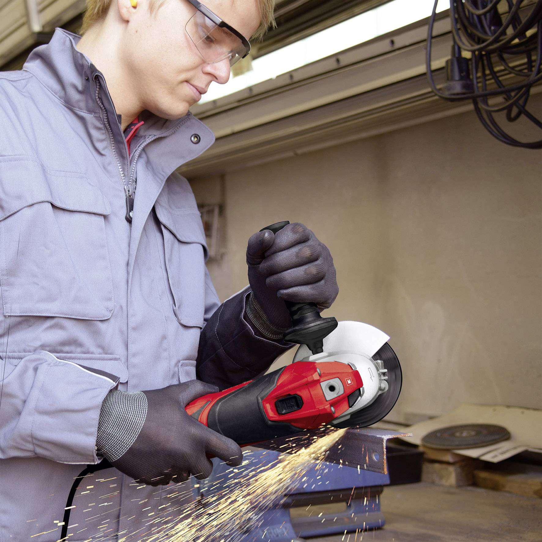 Eine Person schleift mit einem Winkelschleifer Metall. Funken fliegen. Schutzbrille und Handschuhe werden getragen.