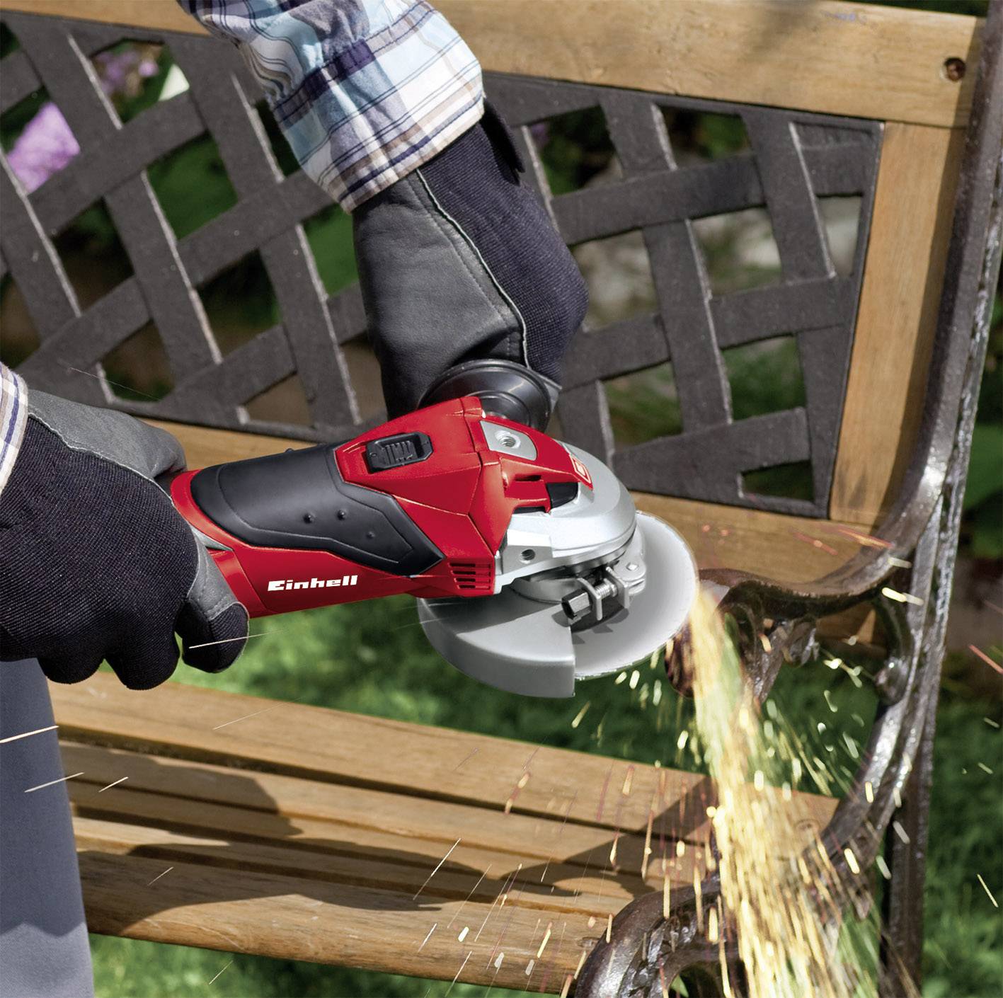 Person schleift mit einem Winkelschleifer einen metallenen Gartenstuhl, Funken fliegen. Schutzhandschuhe und kariertes Hemd getragen.