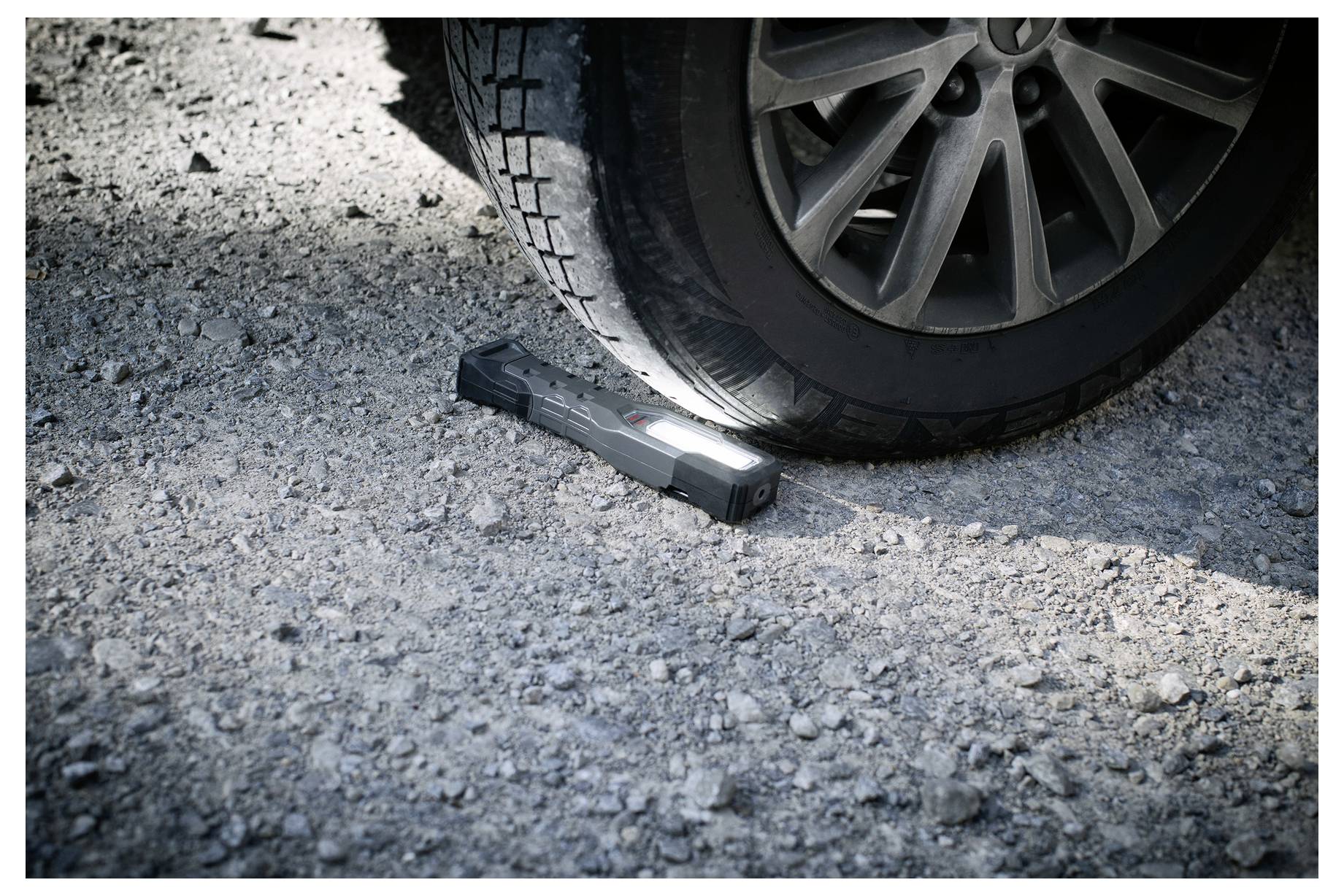 Autoreifen drückt eine Taschenlampe auf einer Kiesstraße fest, was auf eine Panne am Straßenrand oder eine nächtliche Überprüfung hindeutet.
