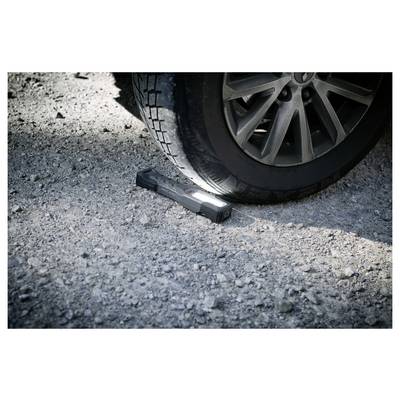 Autoreifen drückt eine Taschenlampe auf einer Kiesstraße fest, was auf eine Panne am Straßenrand oder eine nächtliche Überprüfung hindeutet.