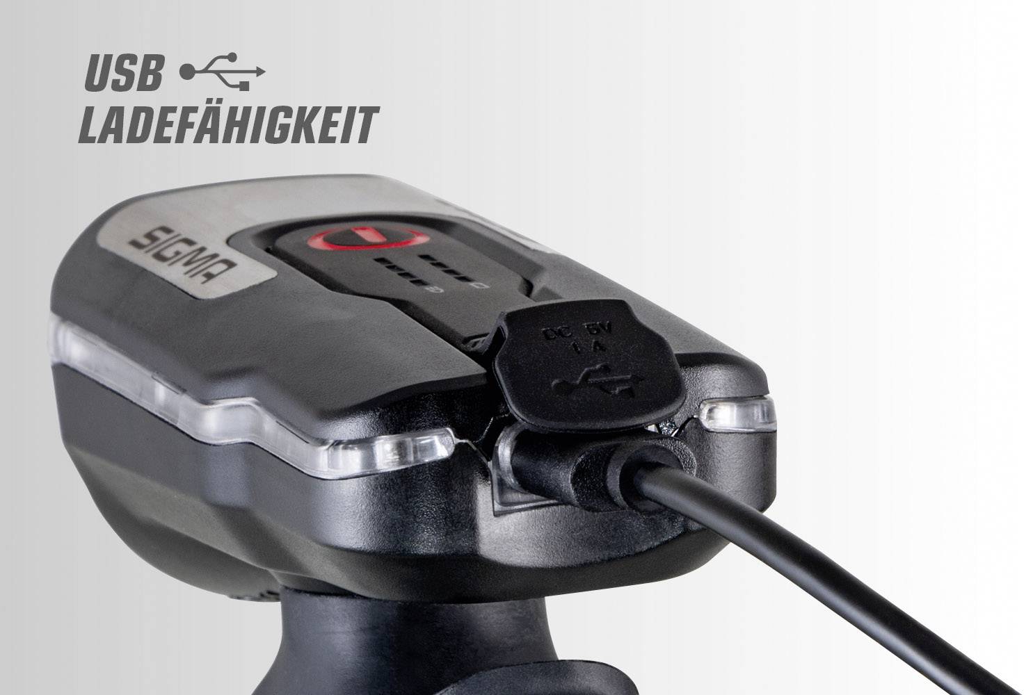 Fahrradlicht mit USB-Ladekabel, schwarzes Gerät mit rotem Knopf und 'USB Ladefähigkeit'-Text, zeigt Ladefunktion.