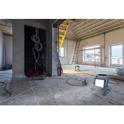 Baustelle in einem Raum mit freiliegendem Dachstuhl, Kabeln, Leiter und Baugerüst. Tageslicht strömt durch große Fenster.