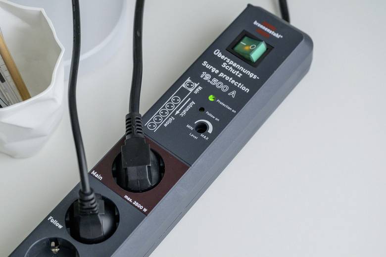 Eine Steckdosenleiste mit Überspannungsschutz und zwei eingesteckten Kabeln. Ein grünes Licht zeigt an, dass sie eingeschaltet ist.