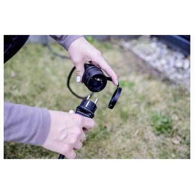 Zwei Hände trennen einen schwarzen Stromstecker, wobei eine Hand die Steckdose hält und die andere den Stecker im Freien auf Gras.