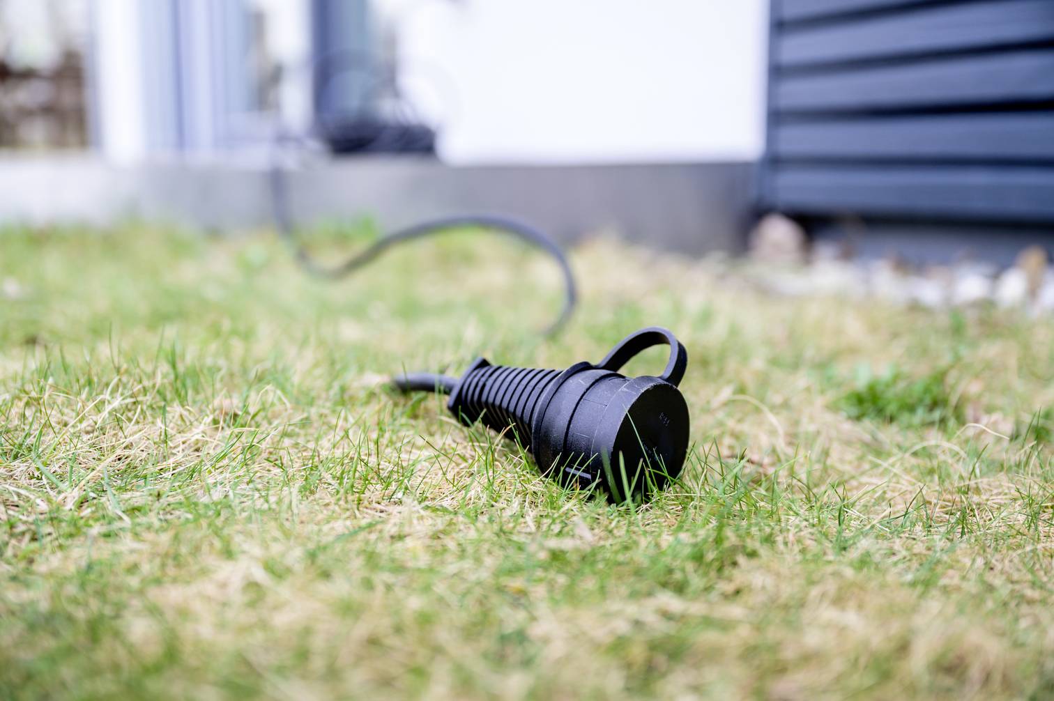 Ein schwarzes Elektrokabel liegt auf einem Rasen, das Bild zeigt einen unscharfen Hintergrund mit einem Gebäude am Rand.