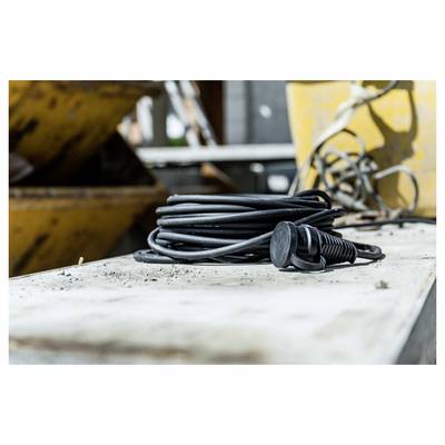 Aufgerolltes schwarzes Elektrokabel mit Stecker, das auf einer staubigen Werkbank in einer Industriewerkstatt ruht.