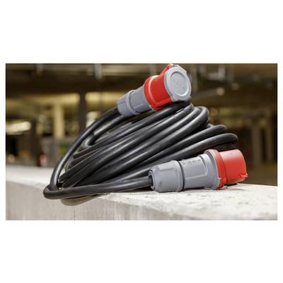 Aufgerolltes schweres Elektrokabel mit roten und grauen Industriesteckern auf einer Betonleiste ruhend.
