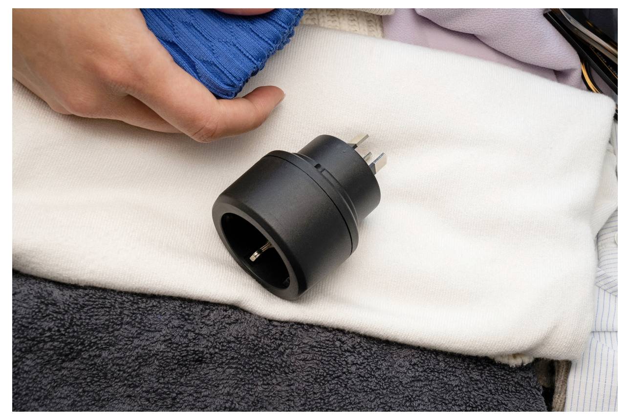 Eine Hand in einem blauen Gipsverband ruht neben einem schwarzen Stromstecker-Adapter auf einem weißen Handtuch, was auf Verletzungspflege oder Genesung hindeutet.
