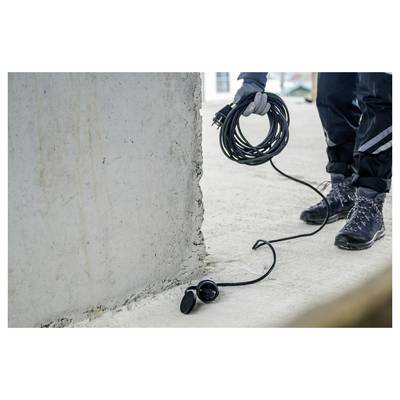 Arbeiter, der ein aufgerolltes Kabel neben einer Wand hält, wobei das Kabel zu einem Gerät auf dem Boden führt.