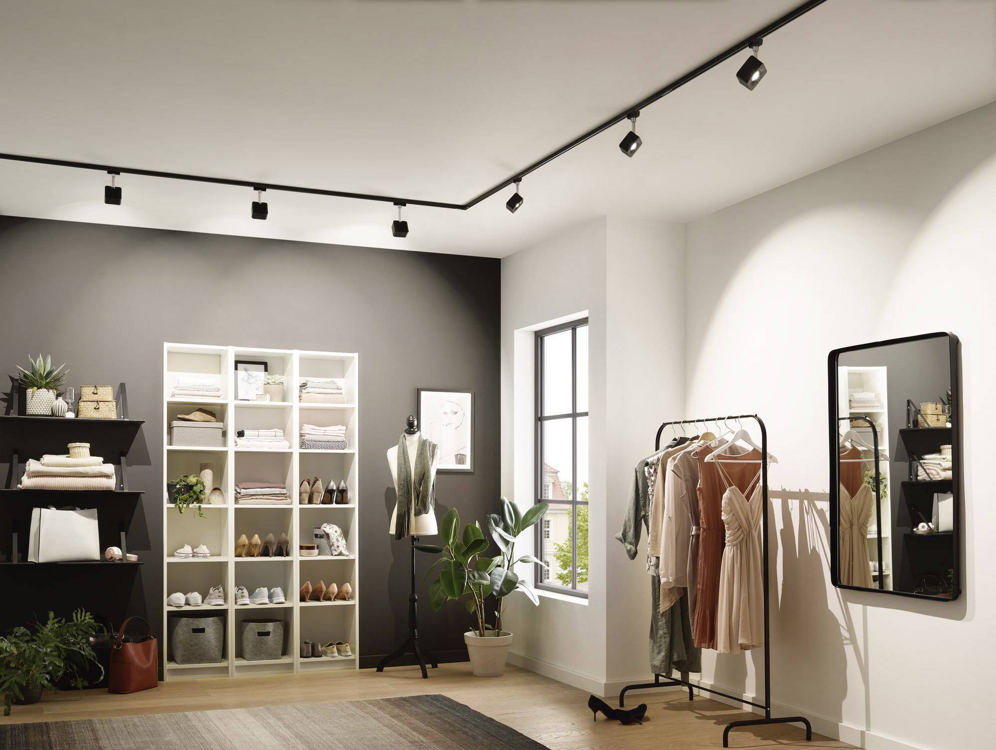 Kleidungsgeschäft mit eleganter Damenmode auf Kleiderständern, Regale mit Accessoires und Pflanzen. Schaufenster mit Licht.