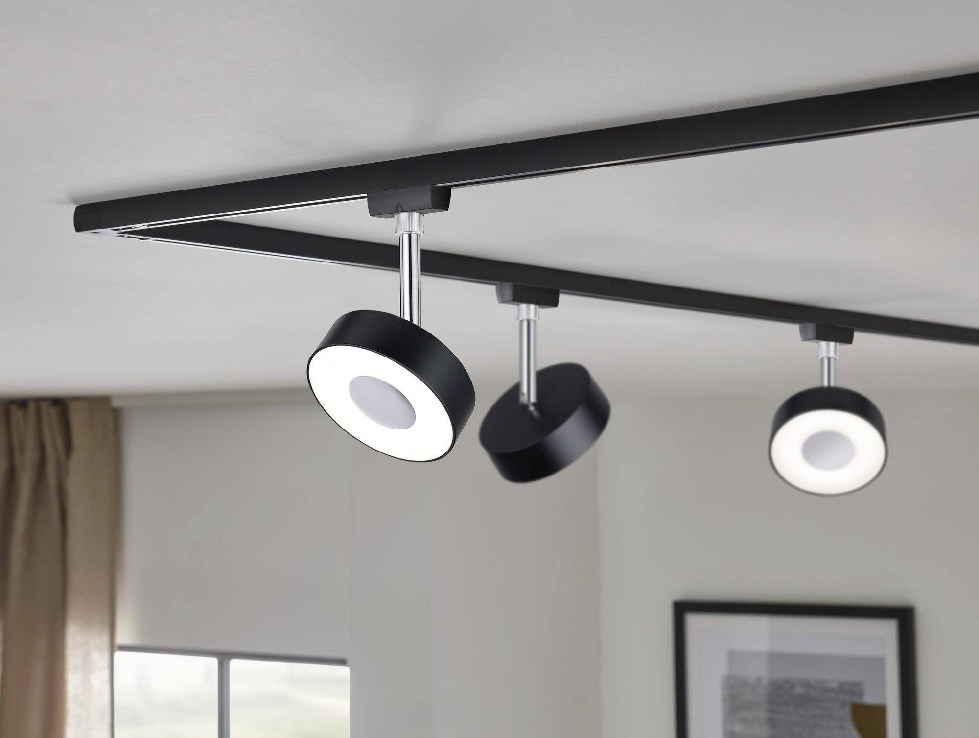 Schwarzes Schienensystem mit drei runden, verstellbaren Deckenleuchten an einer weißen Decke in einem modern eingerichteten Raum.