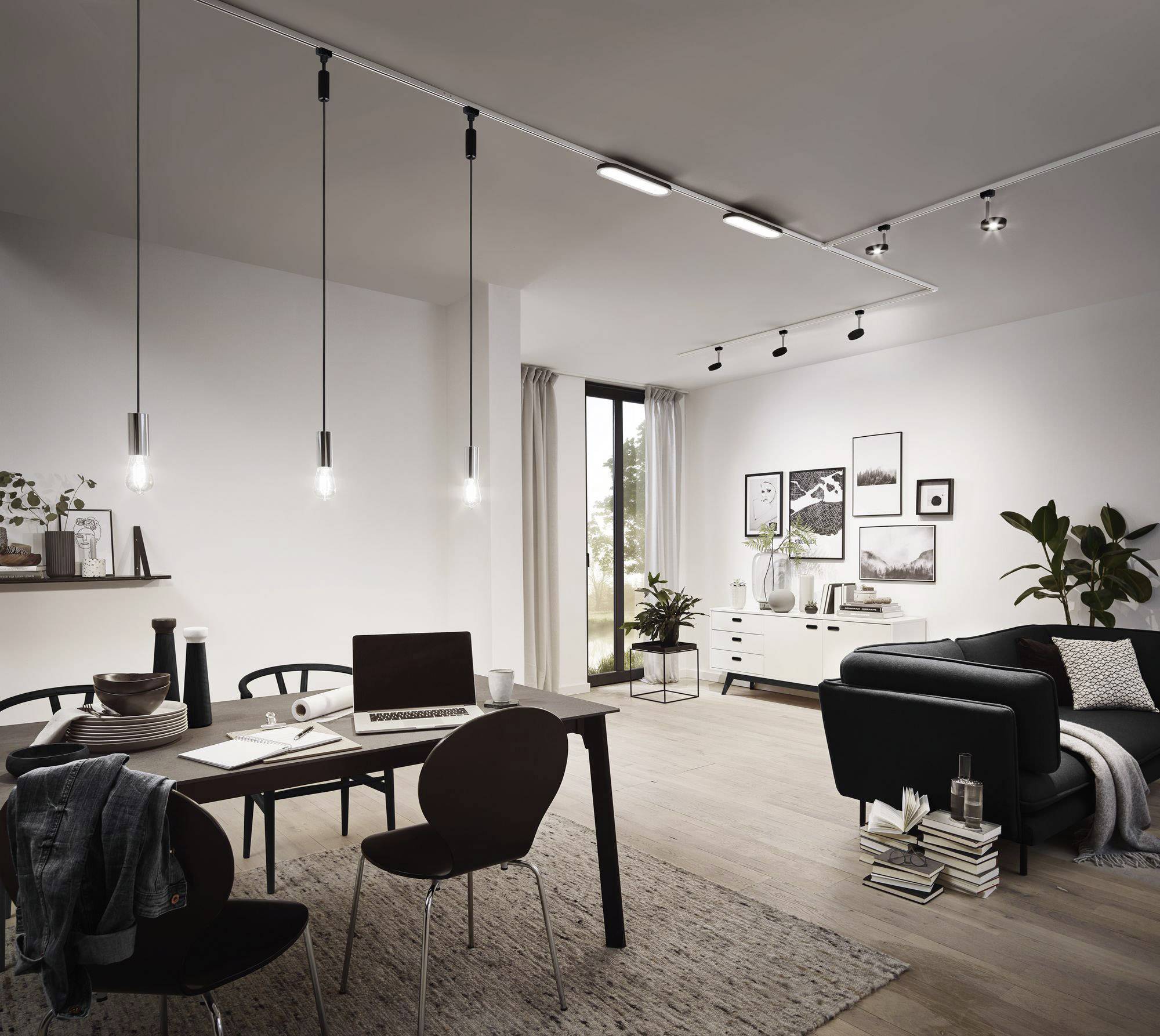 Gemütliches Wohnzimmer mit modernem Essbereich, dunkelgrauem Sofa, vielen Bildern an der Wand, Pflanzen, und Laptops auf Holzmöbeln.