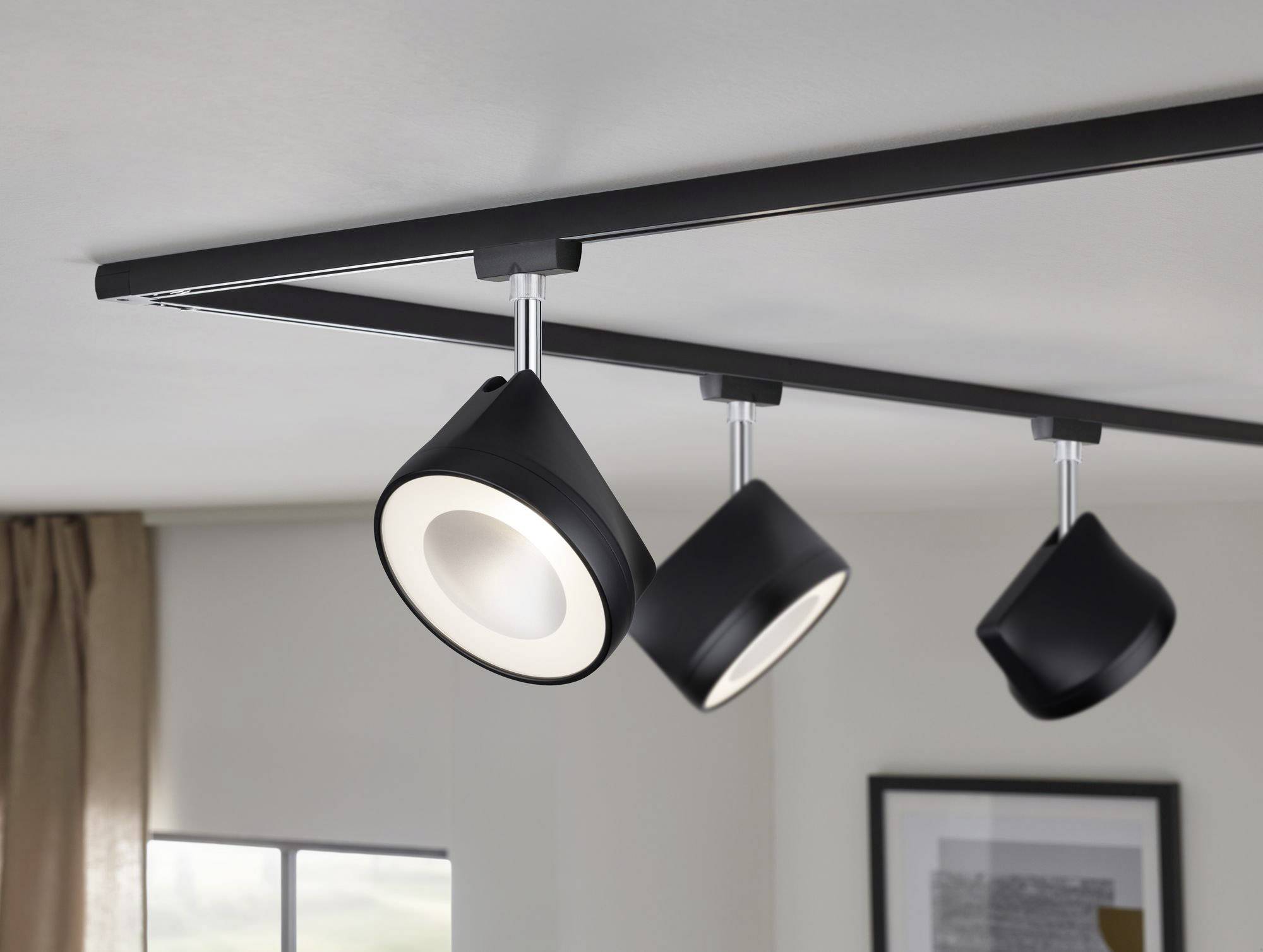 Schwarze Deckenstrahler sind an einer Leiste befestigt und in verschiedene Richtungen ausgerichtet, beleuchten den Raum gleichmäßig.