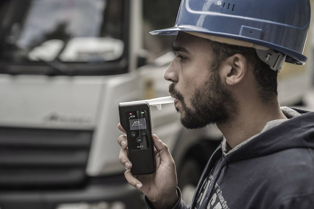 Ein Mann mit Schutzhelm benutzt ein Atemalkoholmessgerät vor einem Lastwagen.
