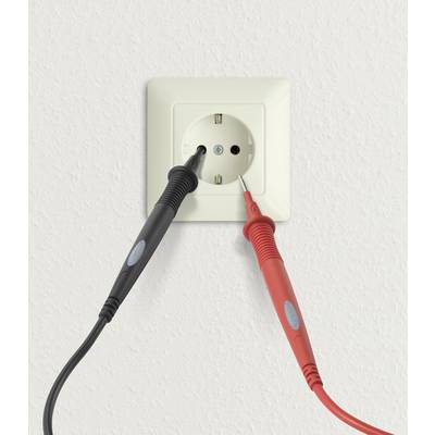 Ein Strommessgerät mit roten und schwarzen Kabeln misst Spannung an einer weißen Steckdose in der Wand.