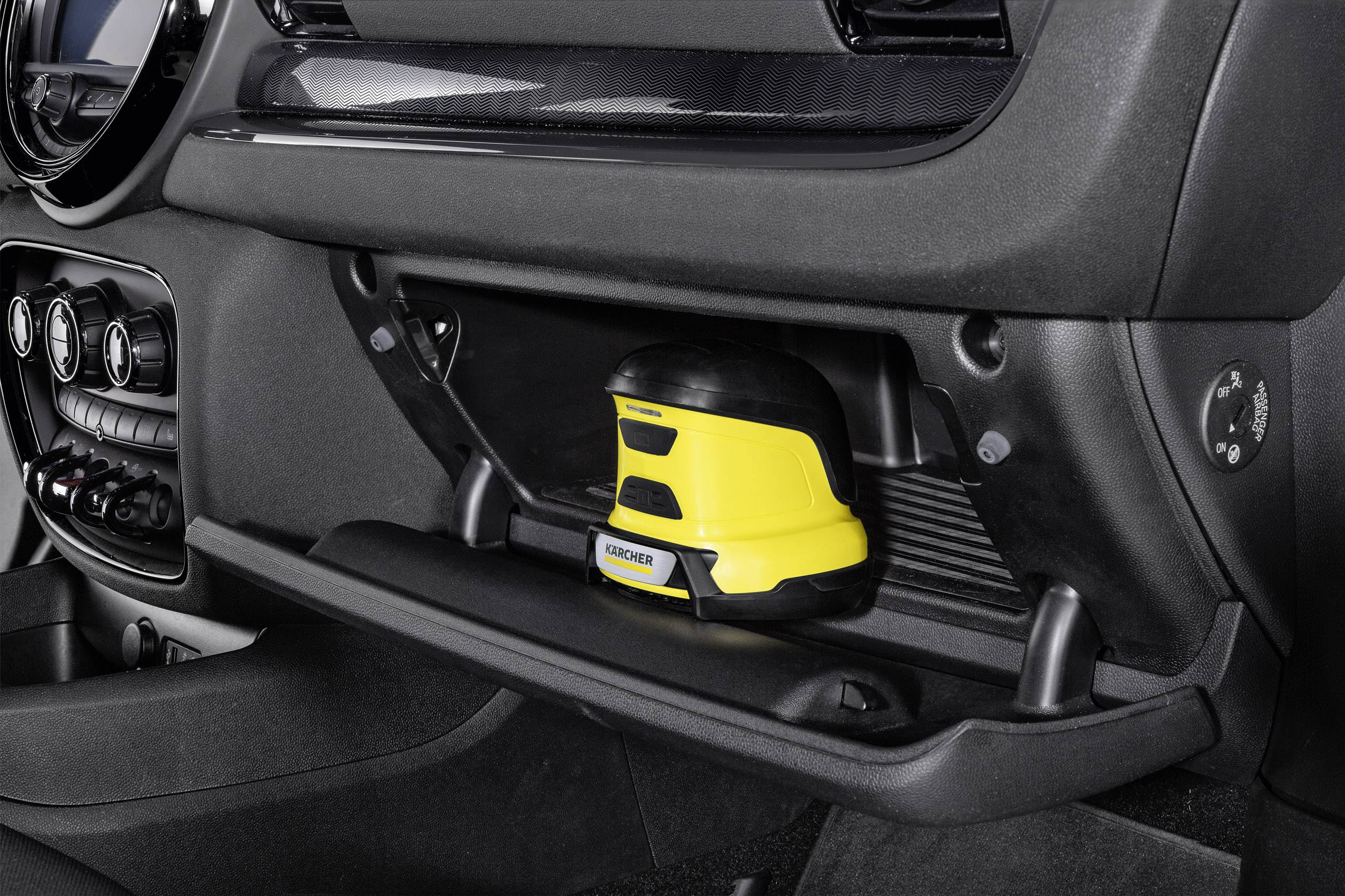 Ein gelbes Gerät befindet sich im Handschuhfach eines Autos, neben Klimakontrollknöpfen. Es scheint für Reinigung oder Wartung gedacht.