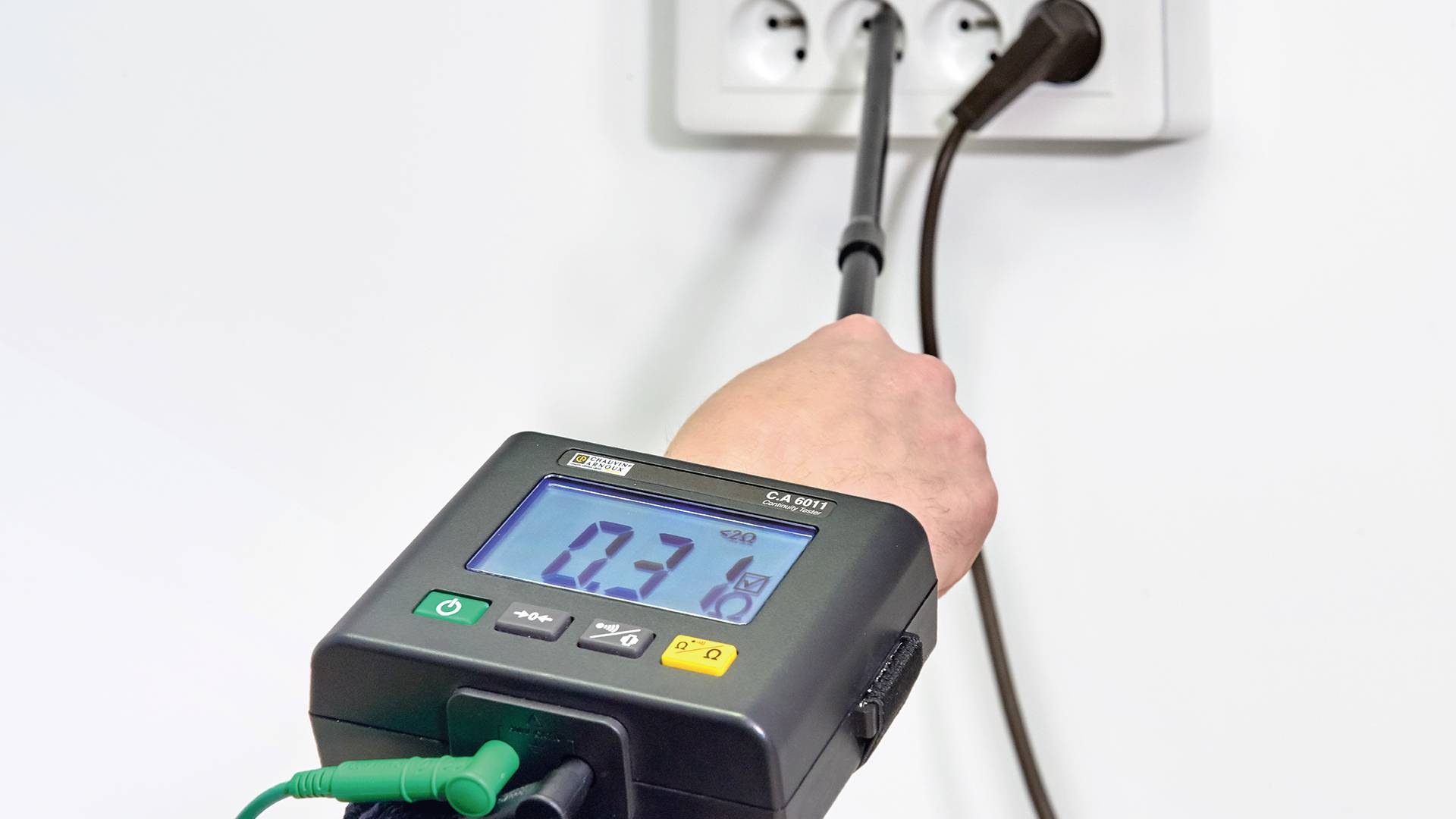 Eine Person testet mit einem Messgerät die elektrische Spannung einer Steckdose. Das Display zeigt '0,3' an.