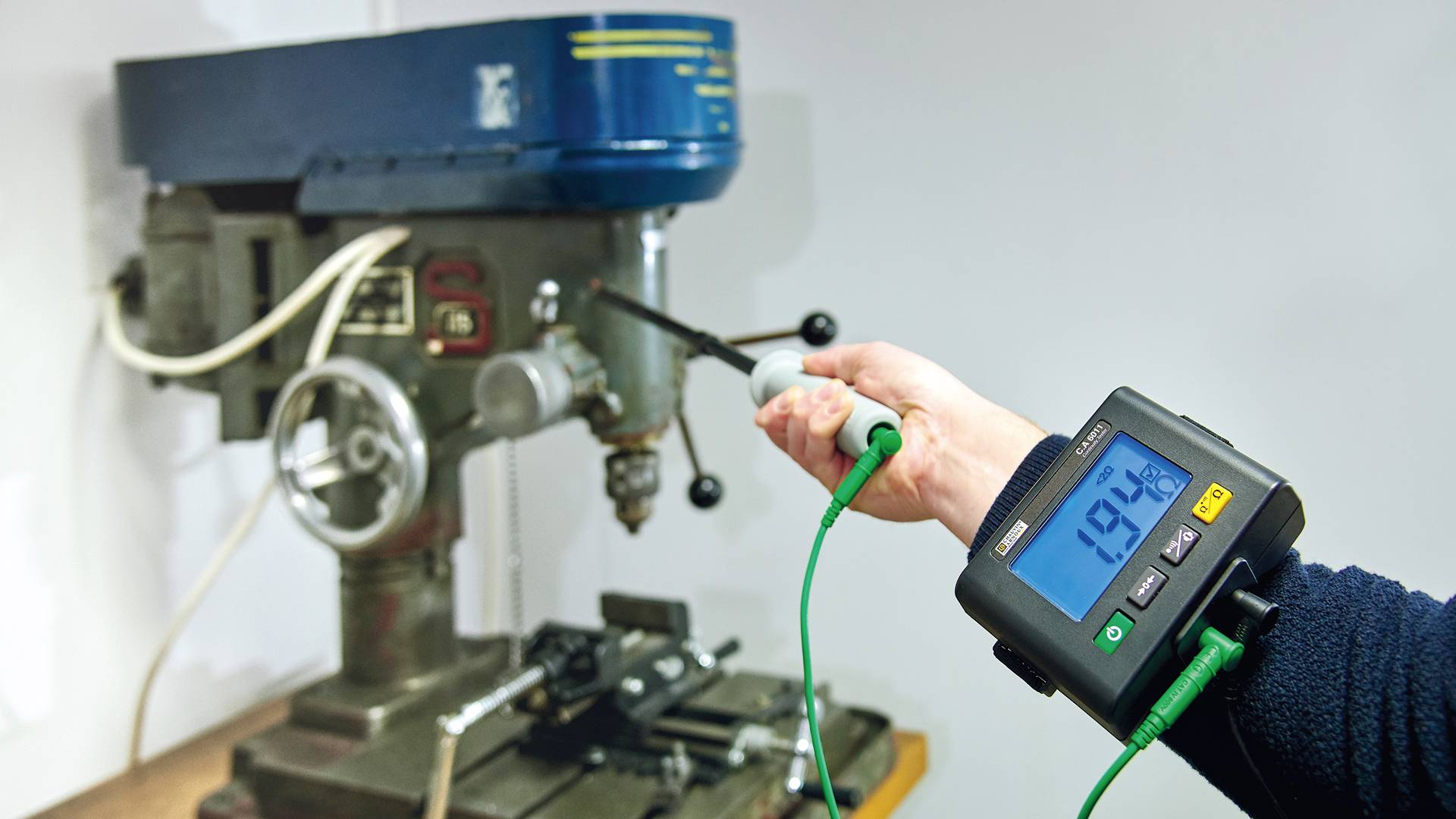 Eine Person misst die Vibration einer Bohrmaschine mit einem digitalen Messgerät. Die Anzeige zeigt einen Wert von 19,6 Hz.