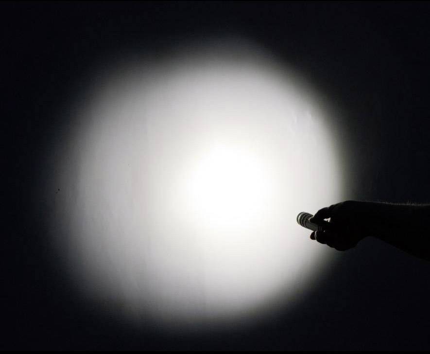 Eine Hand hält eine Taschenlampe, die Licht auf eine Wand projiziert und einen hellen Kreis im Dunkeln erzeugt.