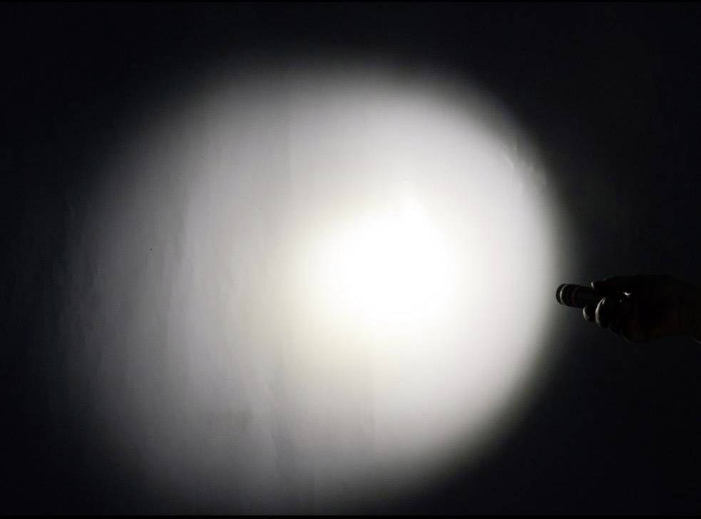 Eine Hand hält eine Taschenlampe, die einen runden Lichtkegel auf eine ansonsten dunkle Wand wirft.