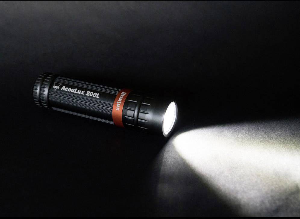 Taschenlampe leuchtet in dunklem Raum. Sie ist schwarz mit einem roten Ring und der Aufschrift 'AccuLux 200L'.