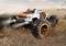 Ein ferngesteuertes Monstertruck-Modell mit großen Reifen fährt über einen staubigen Pfad und wirbelt Schmutz auf.