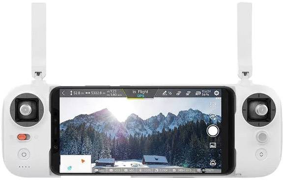Ein Fernbedienungscontroller mit einem Smartphone-Bildschirm, der eine Drohnenaufnahme mit verschneiten Bergen und Wald zeigt.