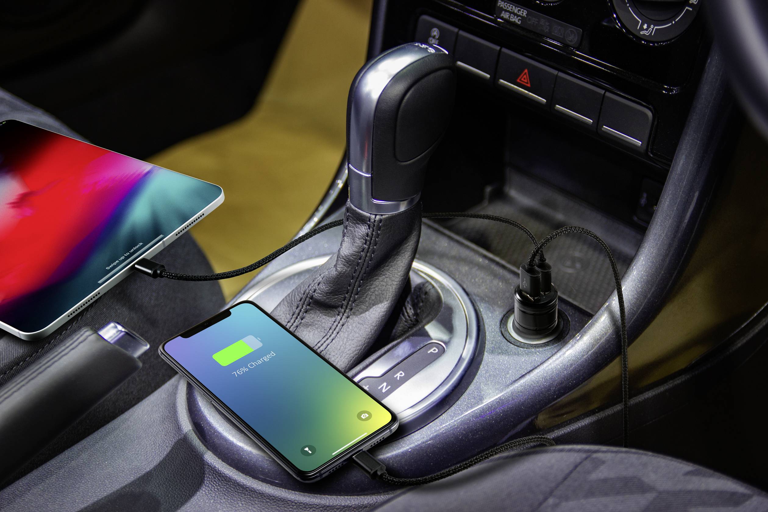 Ein Smartphone und ein Tablet laden im Auto an Ladeanschlüssen in der Mittelkonsole auf. Beide Geräte zeigen einen Ladevorgang an.